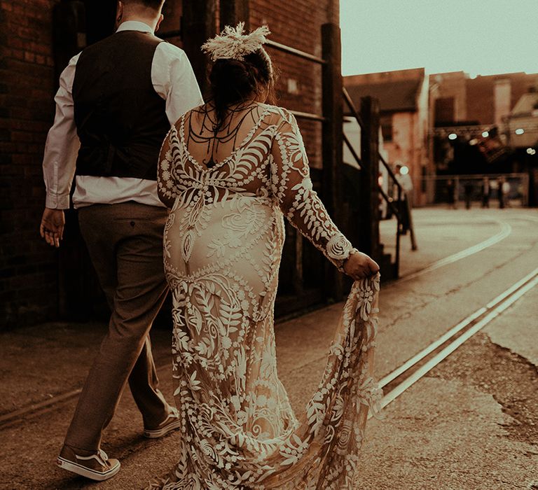 Indian bride in a boho lace Rue de Seine wedding dress with henna on her back walking hand in hand with her groom 