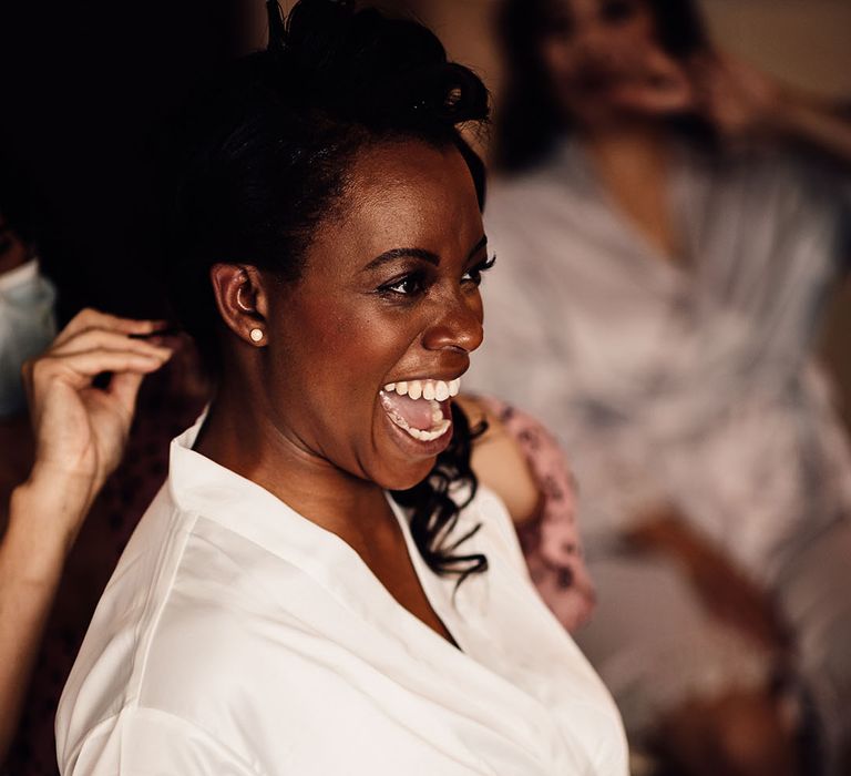 Black bride on her wedding morning in a white getting ready robe drinking champagne 