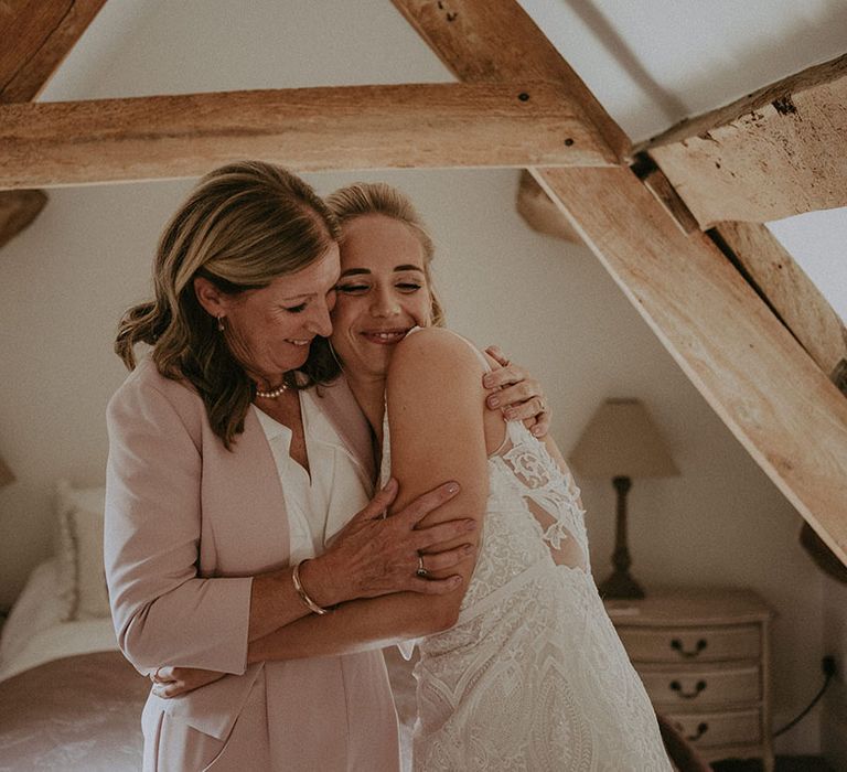 Bride hugs her mother who wears soft muted pink blazer and trouser set 