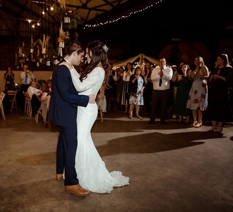 Bride and groom share their first dance with fairy lights and hanging plant decor in the background