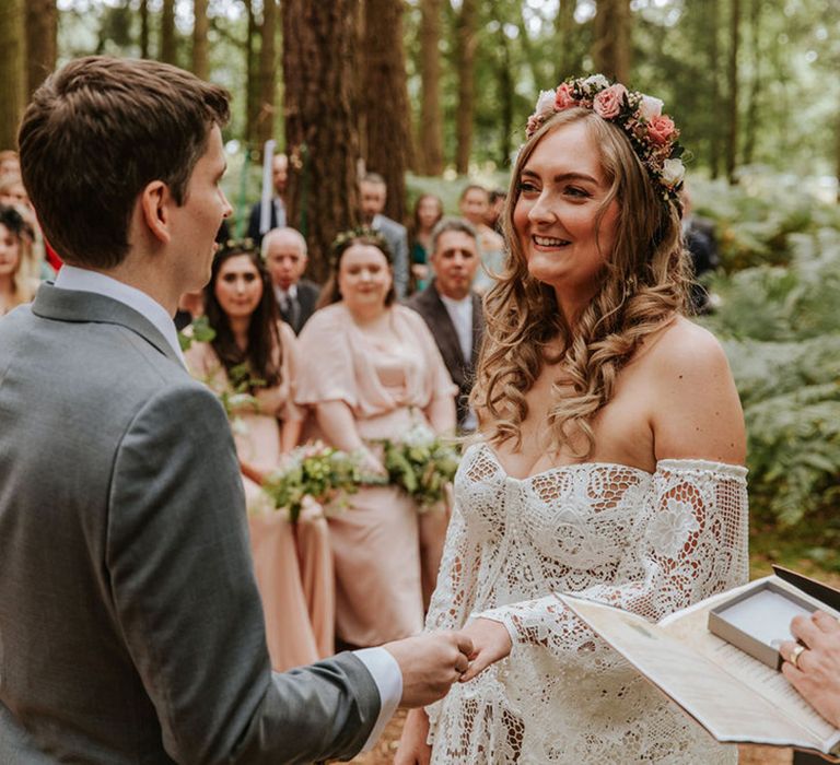 Groom in grey suit puts the wedding ring on the bride's finger wearing a flower crown on curled hair