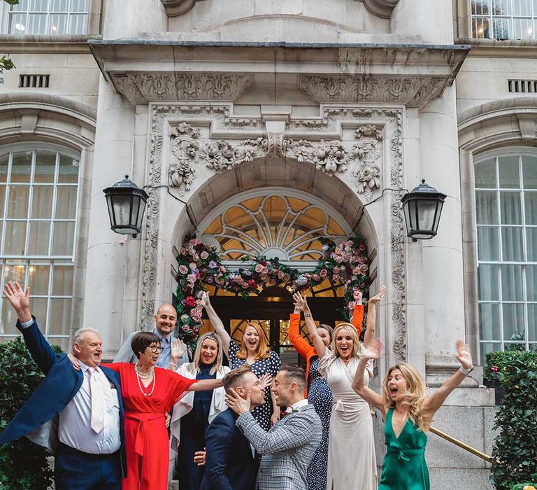 Grooms stand in front of Chelsea Old Town Hall on their wedding day