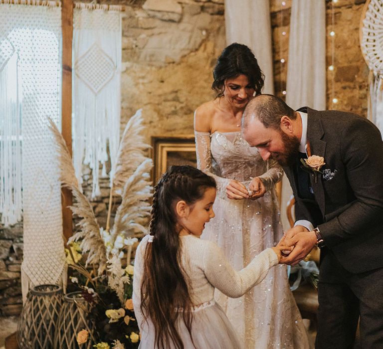 Groom in dark grey suit takes the ring from his daughter for the exchanging of rings