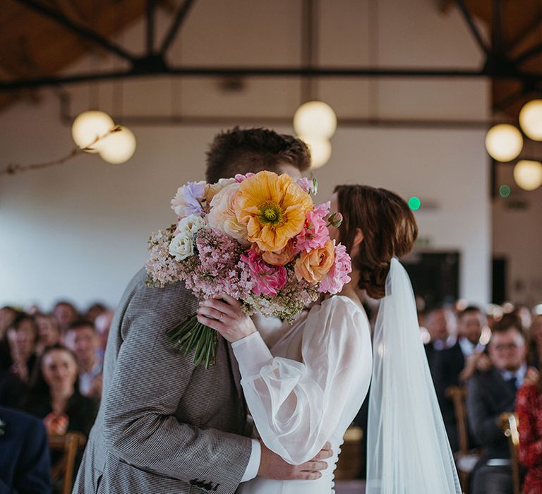 Bride and groom share a kiss as the bride holds the bouquet over their faces with orange giant poppy