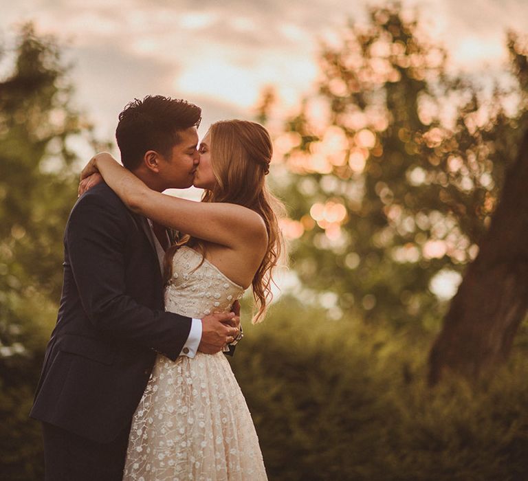 Bride and groom embrace each other as they share a kiss with bride in strapless sparkly wedding dress and groom in blue suit 