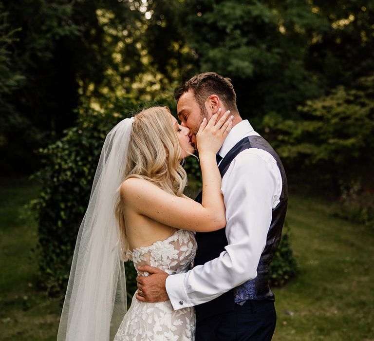 Bride in a Lillian West wedding dress reaches up and kisses the groom 