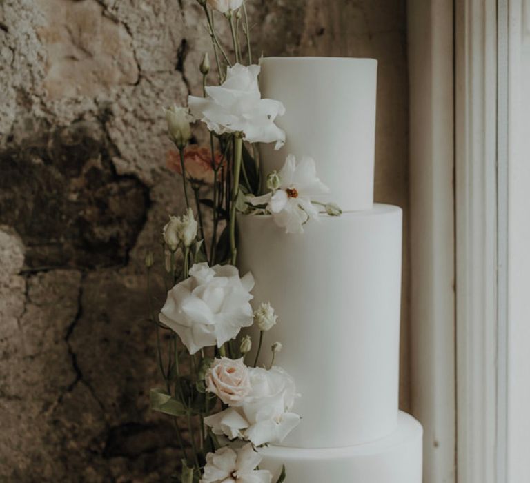 Tall white iced wedding cake with white flowers and greenery 