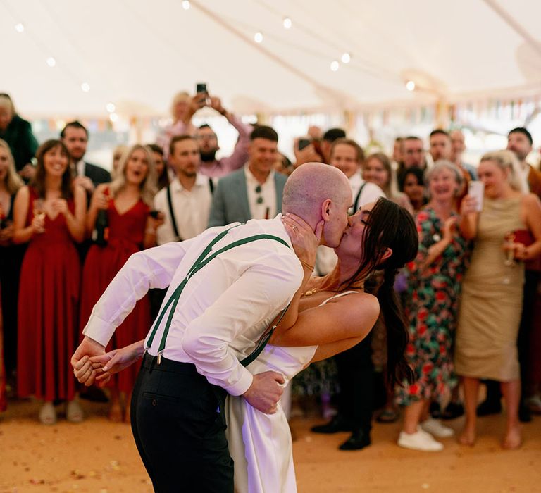 Bride & groom kiss during first dance in marquee wedding as wedding guests watch on