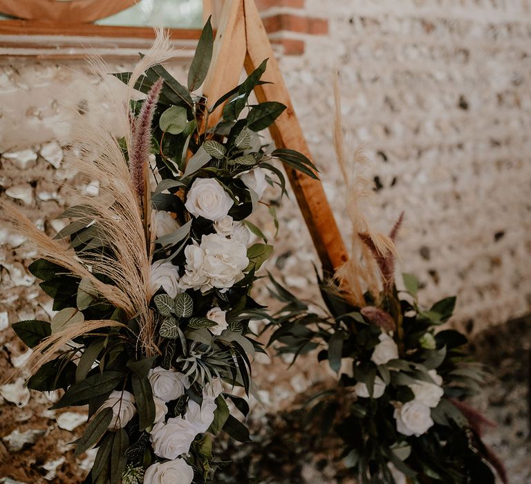 White rose wedding flowers with foliage and dried grass on a wooden arch