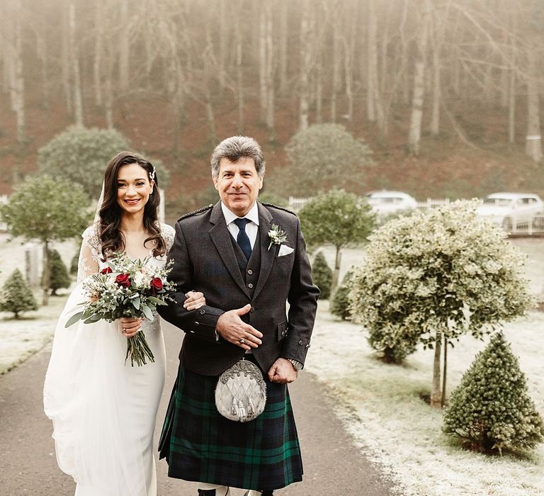 Bride walks with her father outdoors surrounded by snow covered grass and trees in Scotland 