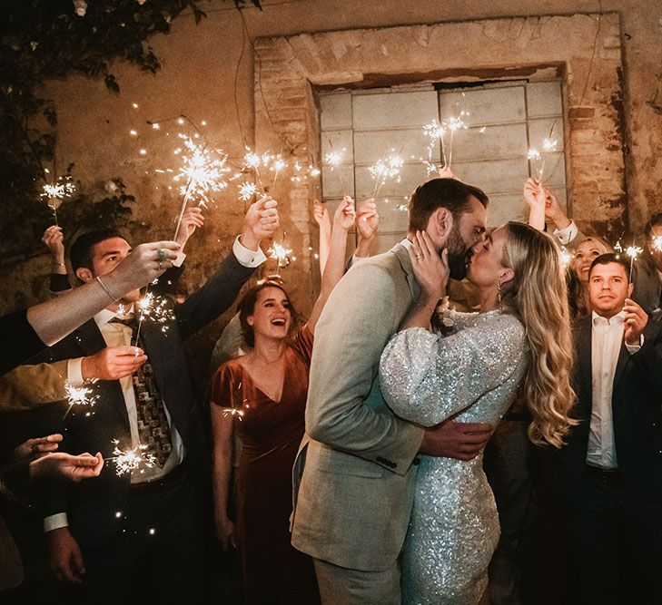 Bride wears silver sparkling short BHLDN wedding dress and embraces groom as wedding guests hold sparklers around them