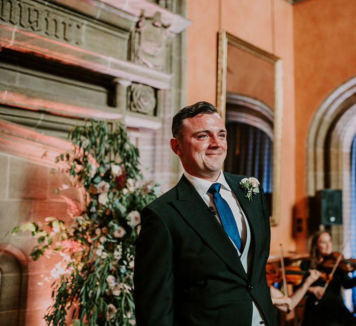 Groom smiles as he sees his bride for the first time walking down the aisle 