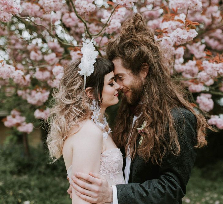 Groom with long hair in a tuxedo kissing his bride in a pink strapless wedding dress