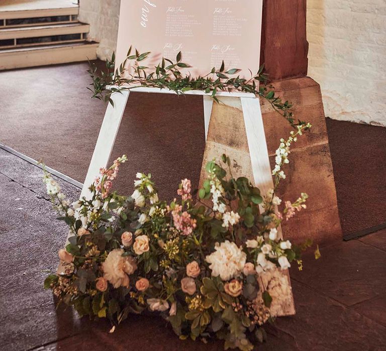 pink seating chart on a white easel with greenery and flower wedding decor 