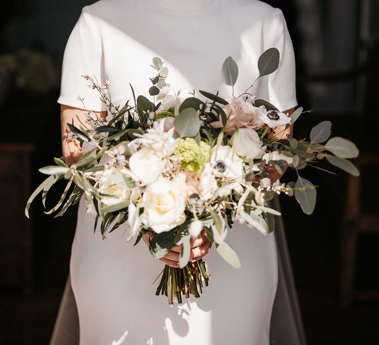 Bride with dainty pearl earrings holding a pink and white bouquet with the bride in a high neck Jesus Peiro wedding dress