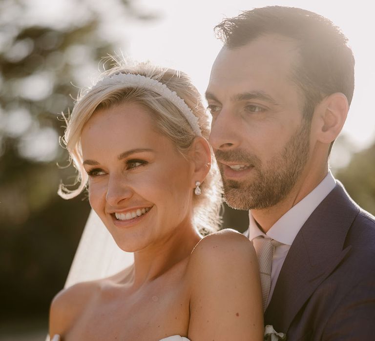 Bride wears Suzanne Neville wedding dress with off-the-shoulder detailing and pearl headband 