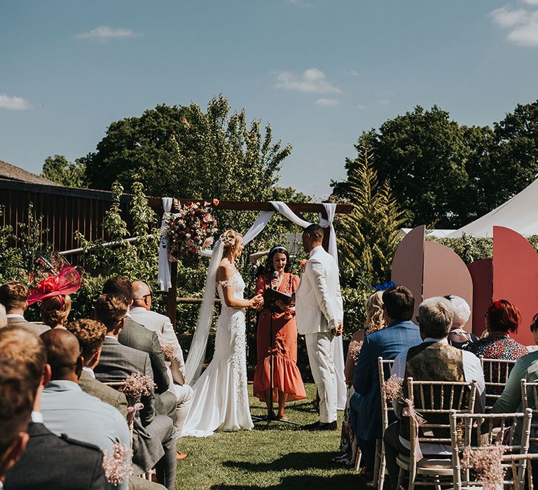 Bride and groom stand for their outdoor wedding ceremony on a sunny day with pink decor 