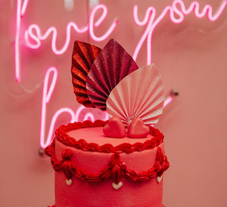 Pink neon sign with a hot pink and red two tier wedding cake with heart and glitter decorations 