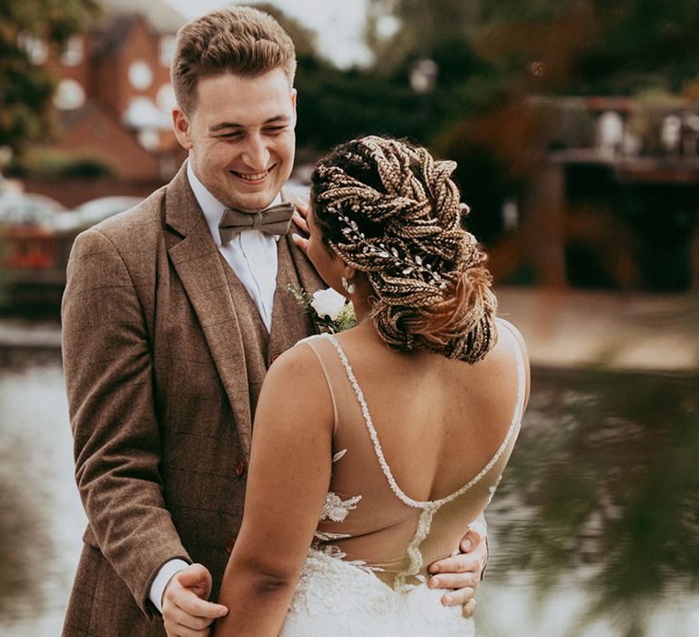 Bride with a sequinned illusion back wedding dress smiling with the groom in a brown checkered suit in front of a lake