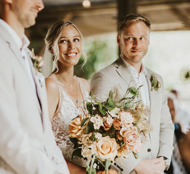 Bride stands at the altar holding her pastel wedding bouquet looking lovingly up at the groom for the ceremony 