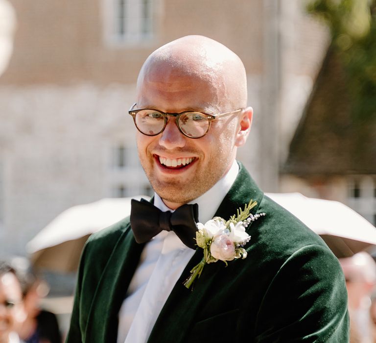 Groom wears black tie green velvet suit jacket and white floral buttonhole 