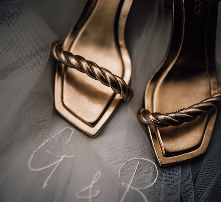 Gold metallic Jimmy Choo wedding shoes resting on top of a veil with personalised embroidered initials and wedding date 