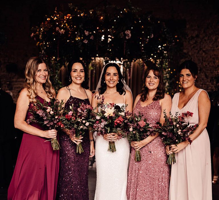 Smiling bride with bridesmaids in mismatched sparkly bridesmaid dresses in shades of pinks and purples 