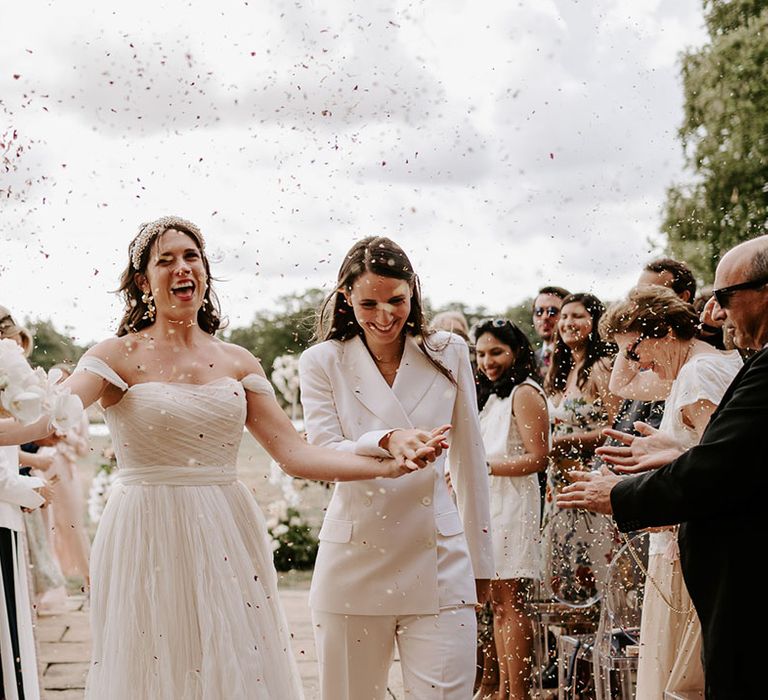 The brides walk holding hands together as they have their confetti moment 