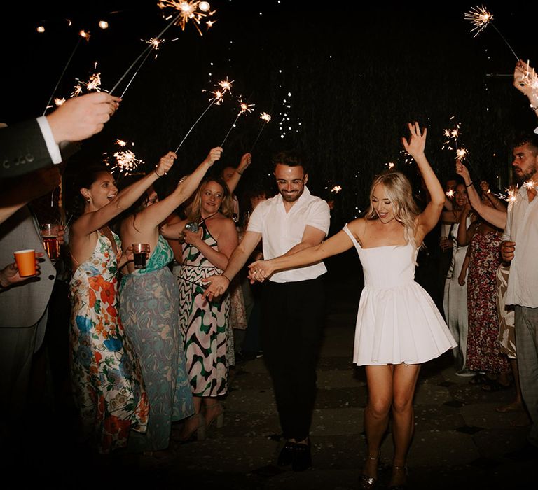 Bride changed into short white wedding dress walking with the groom in a white shirt have a sparkler send off 