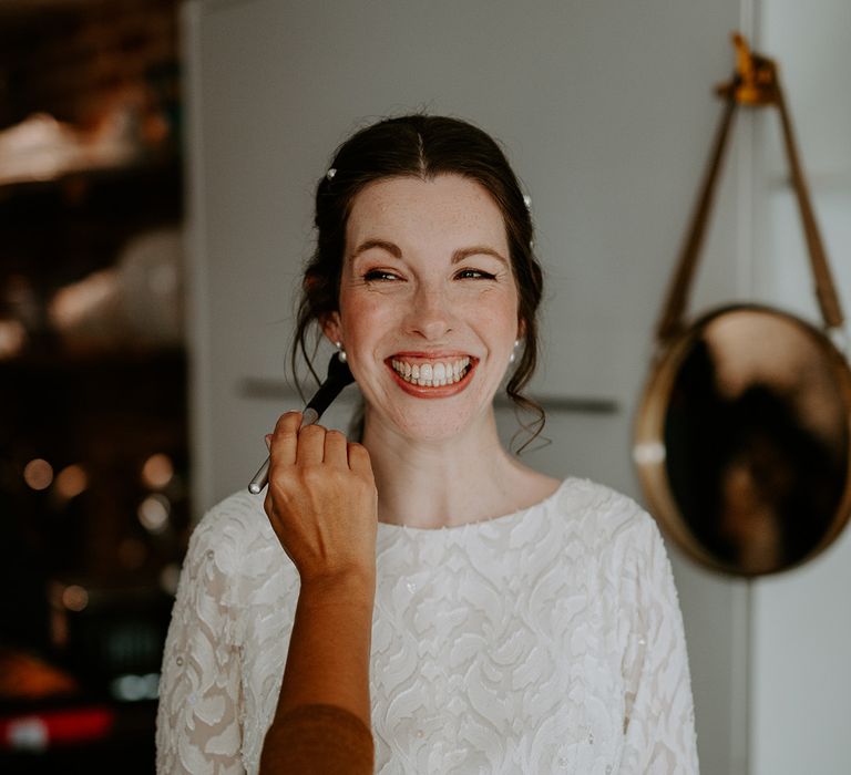 Bride in long sleeve lace vintage wedding dress and closed toe satin heels with pearl earrings and pearl hair clips getting makeup done before autumnal wedding