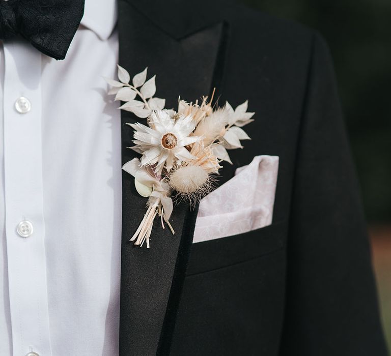 Groom in black tie with a white pocket square and white dried flower buttonhole 