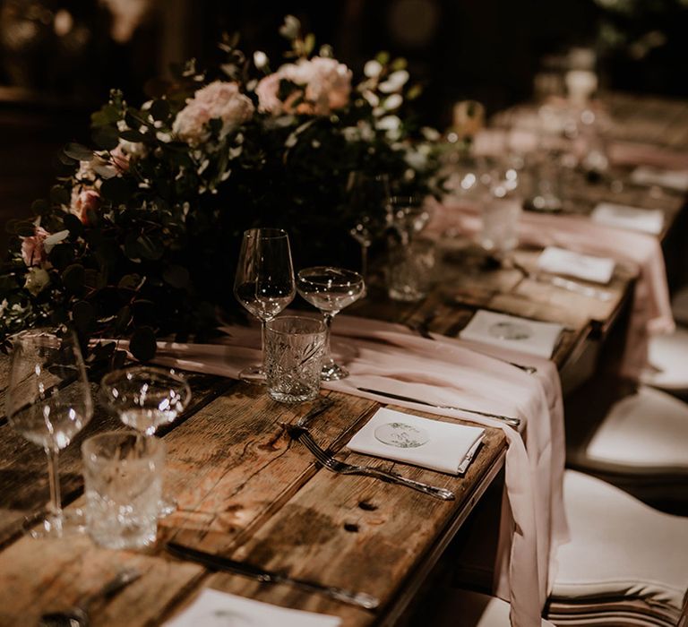 Rustic wooden tables complete with pale pink fabric table runners and floral arrangements 