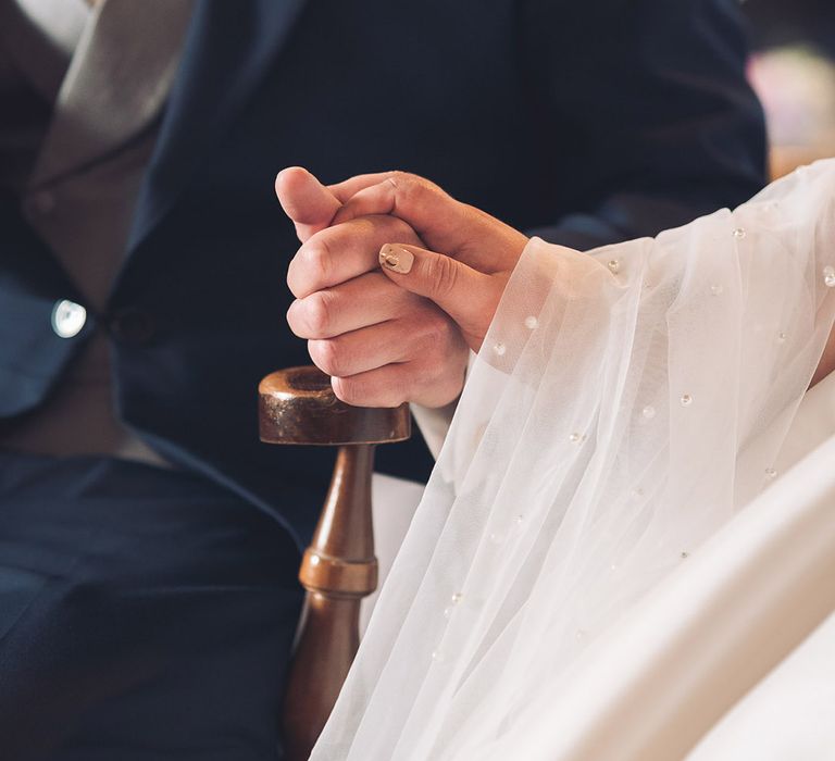 Bride with pale beige nail base colour wit gold moon and stars nail art design with a pearl veil holding hands with the groom in a navy suit