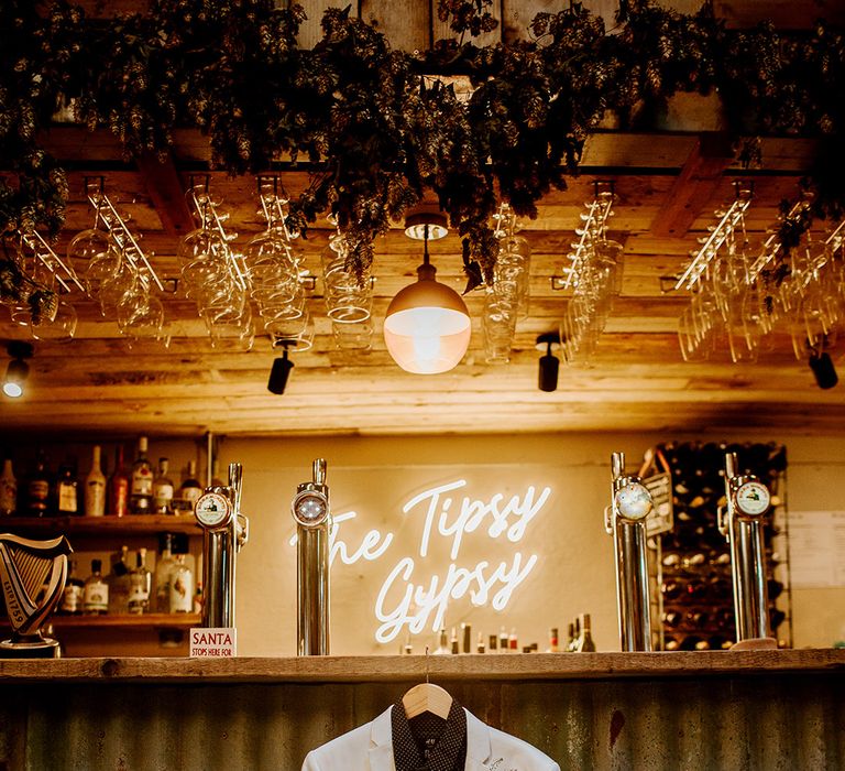 White grooms blazer with colourful boutonniere and black shirt hung up on bar of Kent barn wedding venue 