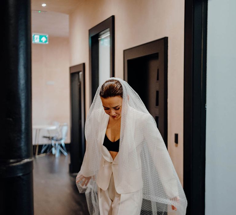 Bride wears white bridal suit with black bandeau top beneath and floor length veil 