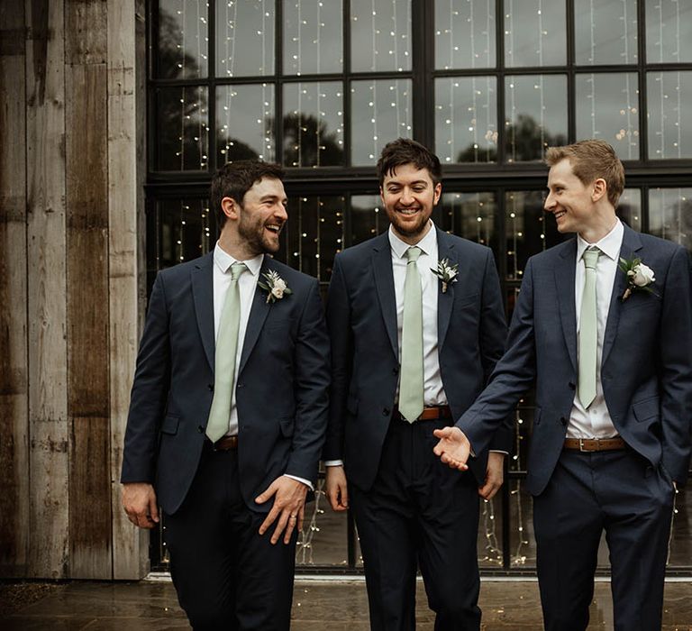 Groom with the groomsmen walking together all in matching navy suits and sage green ties for a rustic luxe wedding 