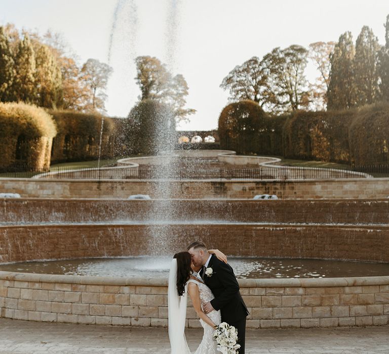 The bride and groom share a kiss in front of a fountain at Alnwick Gardens and Treehouse in Newcastle 