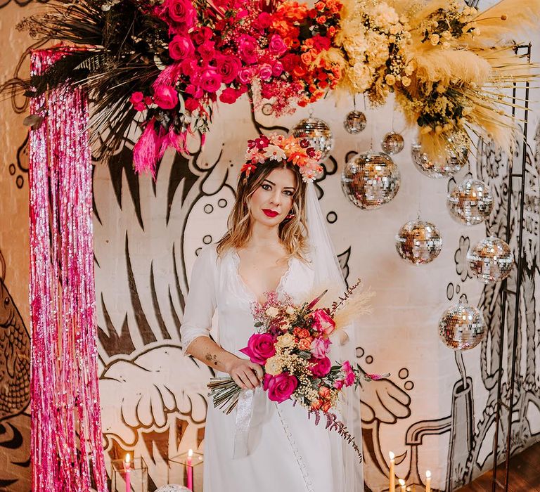 Bride in three quarter length sheer sleeve wedding dress with button and cinched waist details, pink bridal flower crown and pink fluffy open-toe strappy heels holding garden rose, pampas grass, carnations, baby's-breath, dried flower and foliage bridal bouquet with sheer white lace ribbon