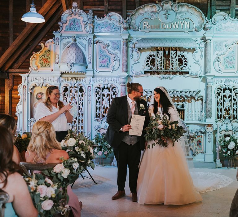 The bride and groom face their guests as a married couple with a vintage pastel pink and blue organ for altar decor at Preston Court 