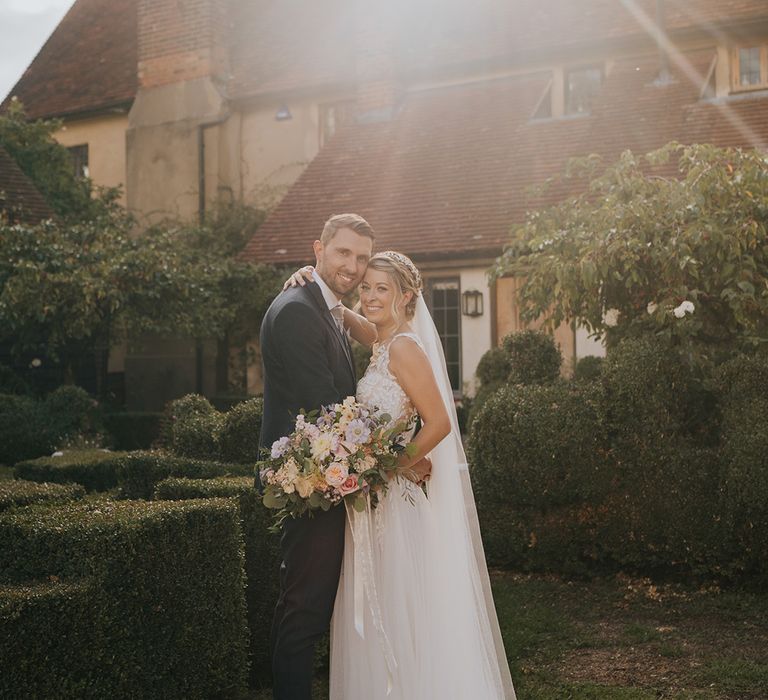 Groom in navy suit embracing the bride in lace and tulle wedding dress during golden hour 