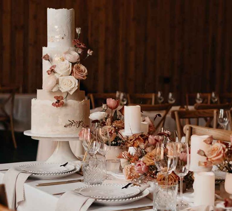 Three tiered buttercream wedding cake with pink dried flower and pearl wedding cake decorations and subtle gold flecks on rustic luxe wedding tablescape with toffee, nude and blush colour palette, soft linen table runners, gold cutlery and charger plates 