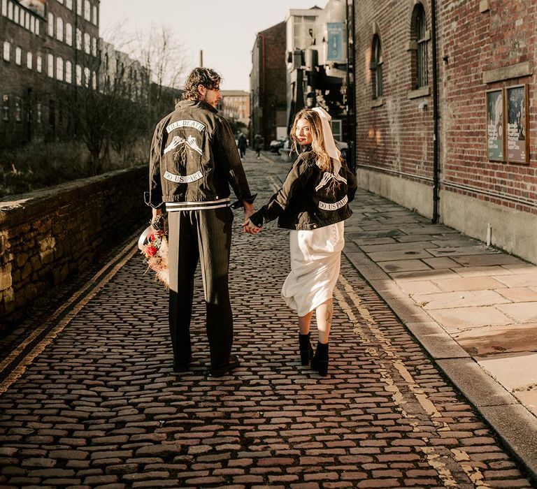 The bride and groom wear matching his and hers black denim jackets with skeleton hands making a pink promise and writing reading 'till death do us part'