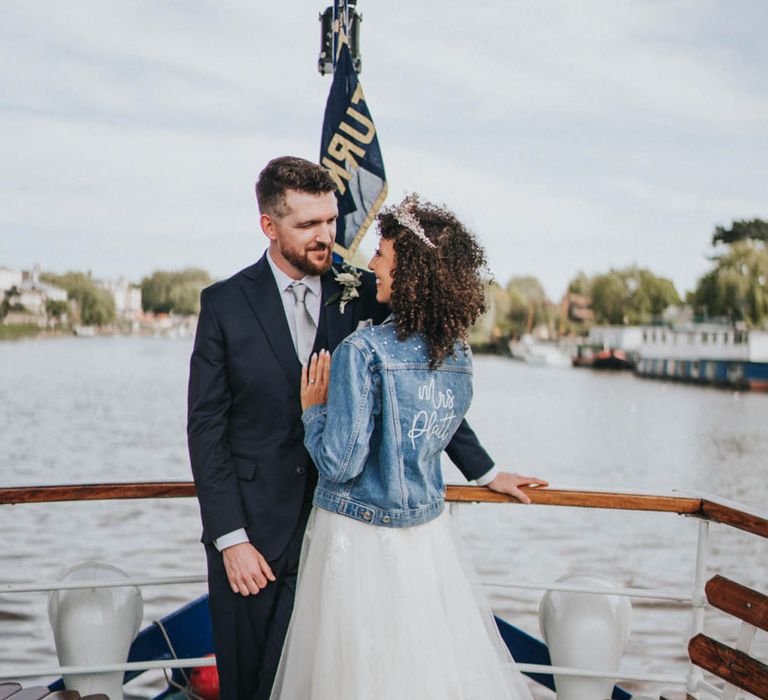 Bride in tulle princess wedding dress with sparkly tiara in personalised pearl denim cover-up with the groom on boat ride 