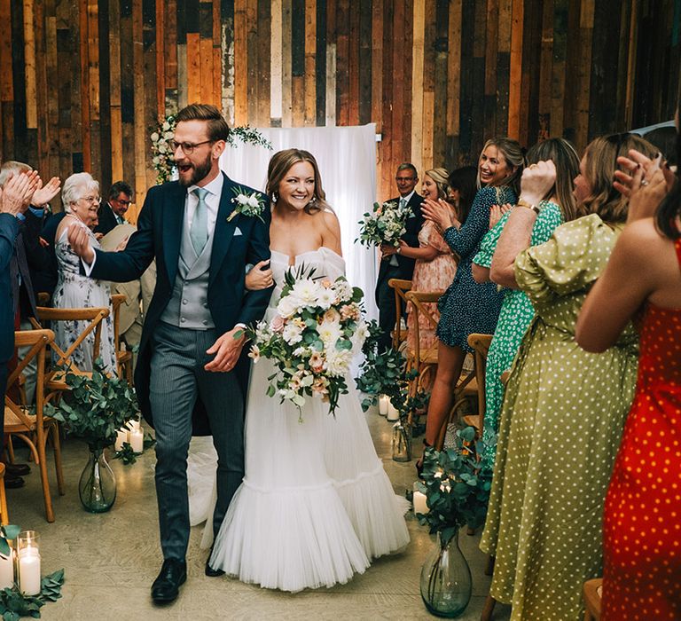 Tulle wedding dress with off the shoulder detail walking back down the aisle with the groom in three piece suit at Willow Grange Farm wedding venue 