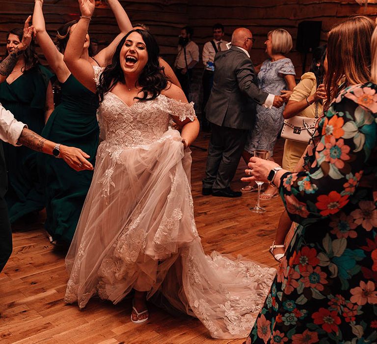 The bride in an off the shoulder wedding gown dances with the wedding guests at the wedding reception 