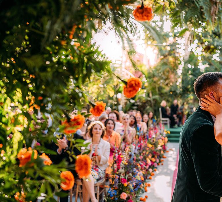 Colourful wedding aisle flowers with floral arch altar decor with the bride and groom sharing their first kiss as a married couple 