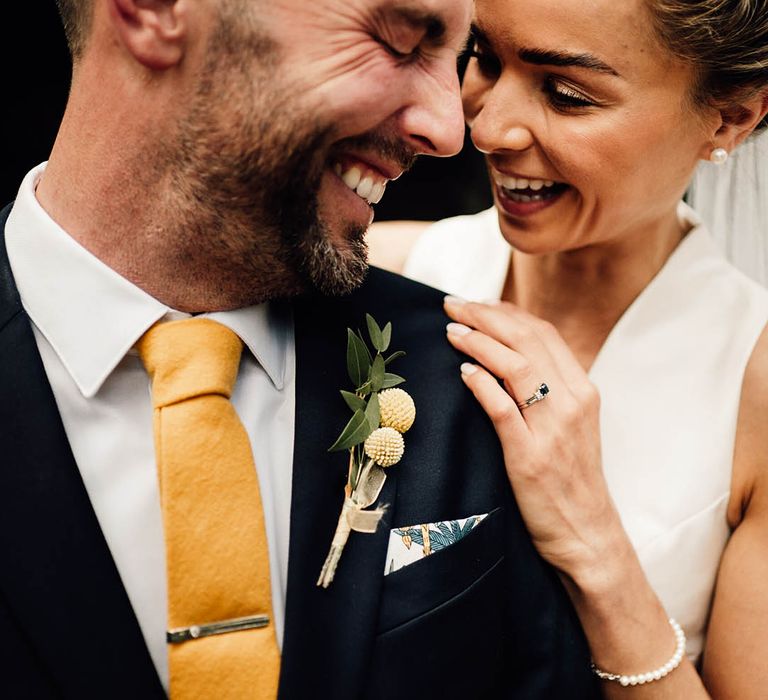 Navy groom suit with yellow tie and tie clip with yellow floral buttonhole and bride in deep plunging neckline wedding dress