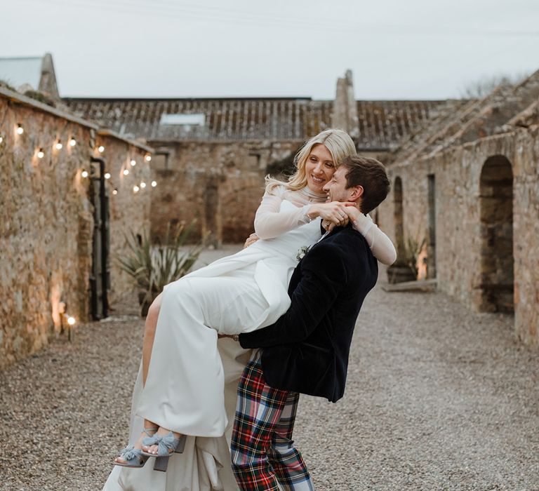 Groom in tartan trousers spins the bride around who wear blue Loeffler Randall wedding shoes 