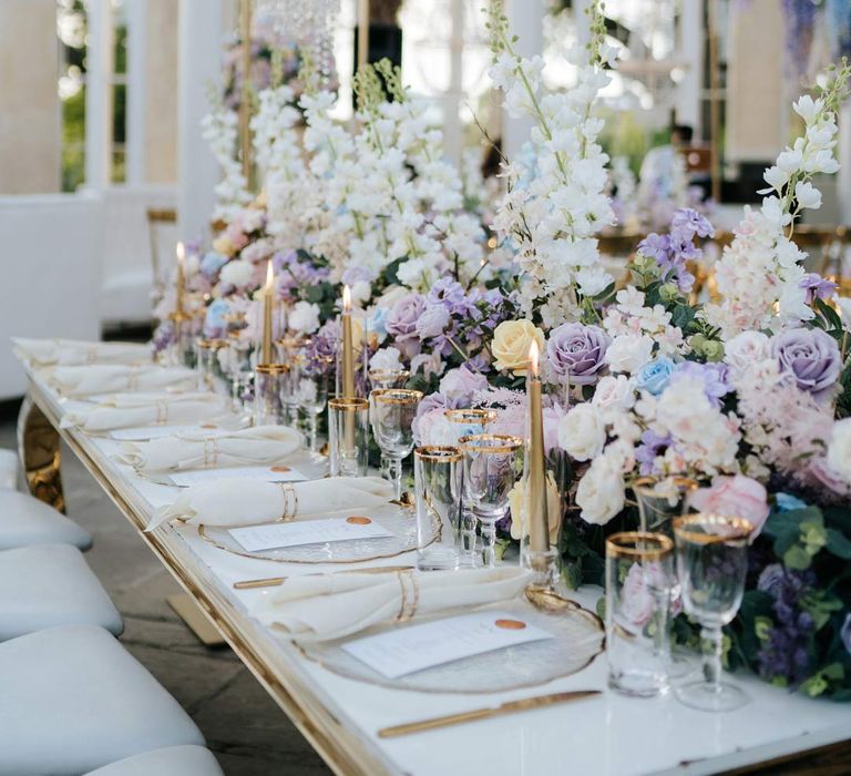 Syon Park wedding venue reception room with gold chairs, botanical tablescapes with large pastel flower centrepieces, gold tapered candles, gold rimmed tableware and suspended pastel foliage decor 