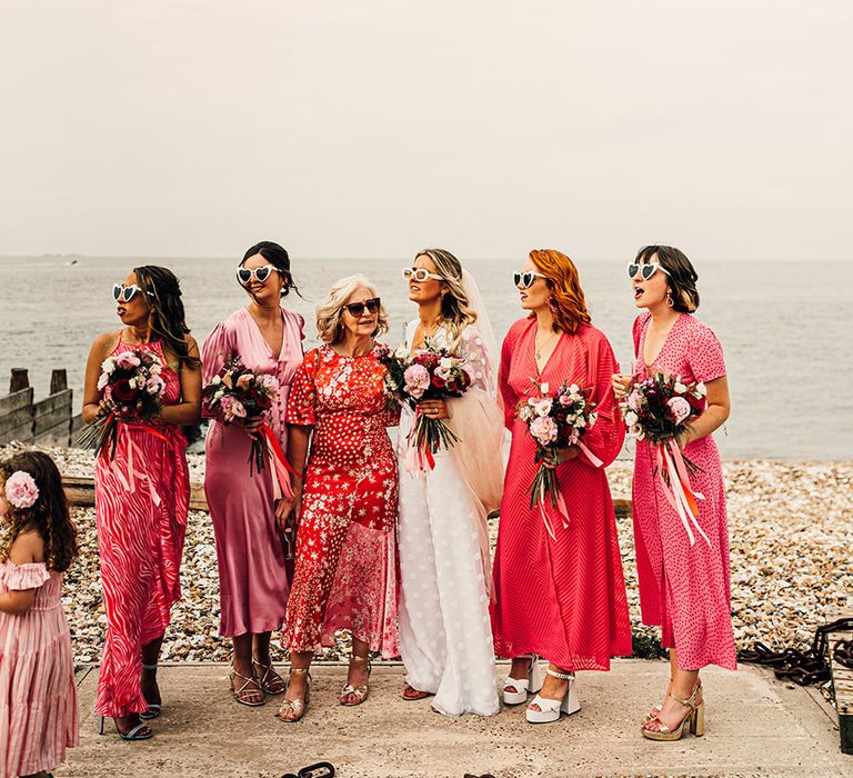 bridal party in different pink bridesmaid dresses at coastal wedding 